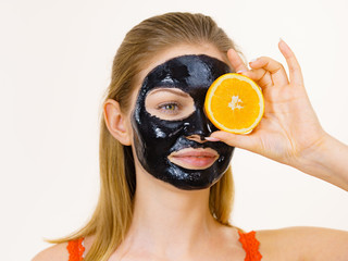 Girl black carbo mask on face holds orange fruit
