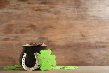 Pot of gold coins, horseshoe and clover leaves on wooden table, space for text. St. Patrick's Day...