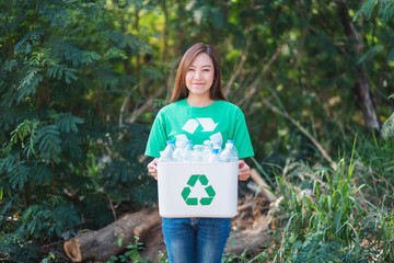 A beautiful asian woman collecting garbage and holding a recycle bin with plastic bottles in the...