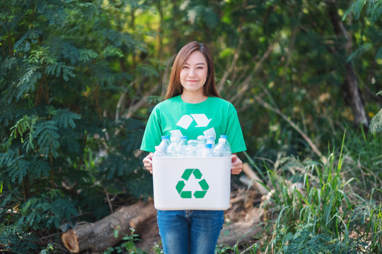 A beautiful asian woman collecting garbage and holding a recycle bin with plastic bottles in the outdoors