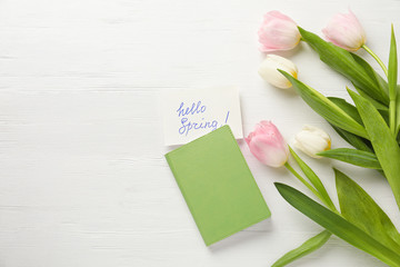 Card with words HELLO SPRING, notebook and tulips on white wooden table, flat lay. Space for text