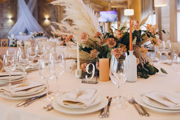on the festive table there are plates with napkins and name cards, glasses, candles, cutlery are lying, there are compositions of flowers