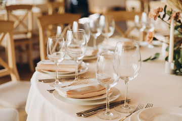 on the festive table there are plates with napkins and name cards, glasses, candles, cutlery are lying, there are compositions of flowers