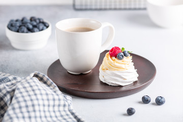 Coffee mug and Pavlova cake with whipped cream and fresh berries on wooden plate. Scandinavian style. Soft focus