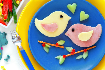 Fun food for kids - cute bird shaped sandwiches or ham and cheese toasts served with vegetables and fresh orange juice. Love birds perching on bread stick branches