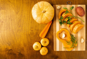 sliced pumpkin with sprigs of dill and parsley on a bamboo cutting Board and other vegetables on a wooden background