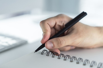 Man writes with a pen in notebook in a sunny office, business and education concept. Close up