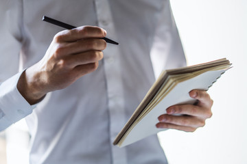 Man writes standing with a pen in diary in a sunny office, business and education concept. Close up