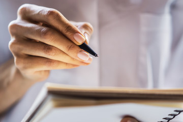 Businesswoman writes standing with a pen in diary in a sunny office, business and education concept. Close up