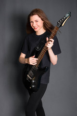 Fototapeta na wymiar Portrait of a beautiful, young rock girl in black clothes with an electric guitar in her hands. Studio photo on a gray background. Model with clean skin.