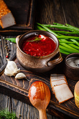 Ukrainian cuisine. Red soup borsch in a clay pot with sour cream and Ukrainian bacon. Serving dishes in a restaurant on a wooden table. background image, copy space text
