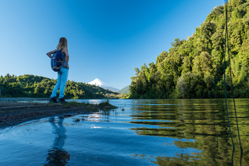 Woman stands on the coast of the blue lake with volcano of Osorno on the background. Patagonia, Chile