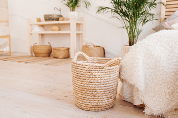 Light interior made of natural ecoy components. Wicker straw basket for storing clothes and things on the background of the washbasin and bath in the Boho style with wicker baskets and wooden shelves