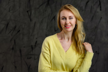 Photo of stylish pretty blonde woman with long hair in a yellow sweater on a gray background