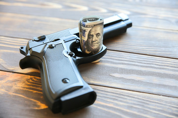Money and gun lying on wooden background. Dollars rule the world. Corrupted world. Greed killing.