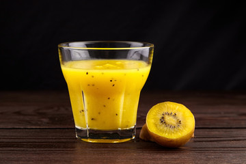 Kiwi gold fruit juice in transparent glass on wooden table on black background. Half of yellow kiwi. Fresh kiwi smoothie. Healthy food and drink
