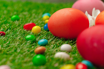 Close up photo of colored Easter eggs and candies on grass
