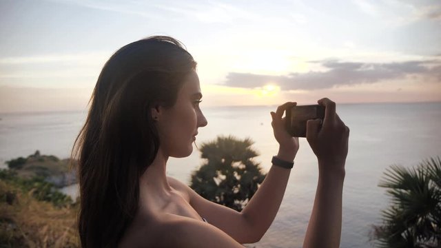 Female hands holding smartphone and doing nature photography. young tourist woman taking photos with mobile phone camera of amazing sunset at the beach.