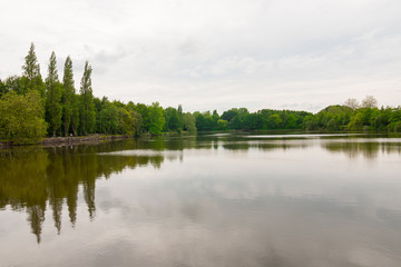 Beautiful lake during the fall season, Flers, Normandy, France. Green foliage in the background that reflects in the water. Cloudy day in the park.