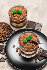 Classic tiramisu dessert in a glass cup and pieces of chocolate on concrete background