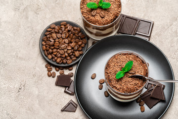 Classic tiramisu dessert in a glass cup and pieces of chocolate on concrete background