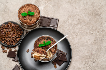 Classic tiramisu dessert in a glass cup and pieces of chocolate on concrete background