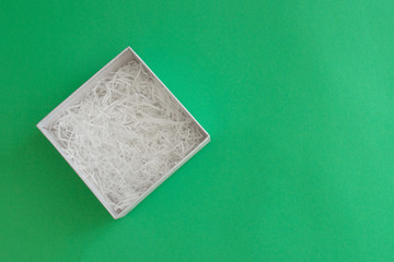 open box with filling material inside lying on a left side of green colored paper background, top view with copy space