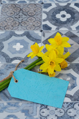 Bunch of daffodils narcissus tied with string with a blank blue label tag on a tiled surface.  Spring Saint David’s Day concept