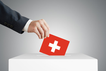 Man putting a voting ballot into a box with Switzerland flag.