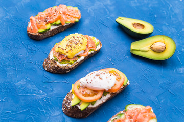 Sandwiches with smoked salmon, eggs, sauce and avocado on blue background. Concept of breakfast and healthy nutrition.
