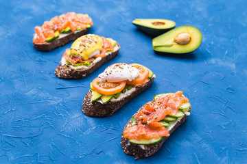 Sandwiches with smoked salmon, eggs, sauce and avocado on blue background. Concept of breakfast and healthy nutrition.