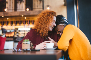 Two female friends laughing out loud in a cafe, having a good time.