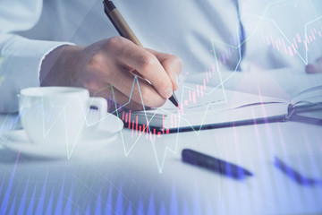 Double exposure of man's hands writing notes of stock market with forex chart.
