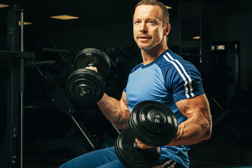 Fototapeta na wymiar Fit senior man exercising with dumbbells in a gym