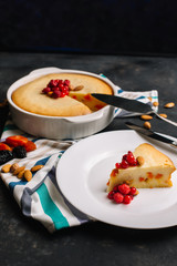 Freshly baked homemade cottage cheese pie with dried apricots, almonds and raspberries. A piece on a white plate decorated with berries and Cutlery side View on a dark background