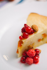 Freshly baked homemade cake with cottage cheese and dried apricots, almonds and raspberries and a glass of milk. A piece on a white plate decorated with berries and Cutlery side View on a dark backgro