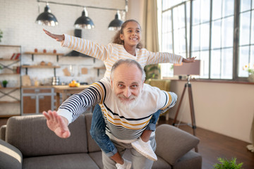 Bearded grey-haired man having fun with his dark-skinned granddaughter
