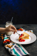 The girl breaks off a piece of cottage cheese pie with berries on a dark background with a spoon