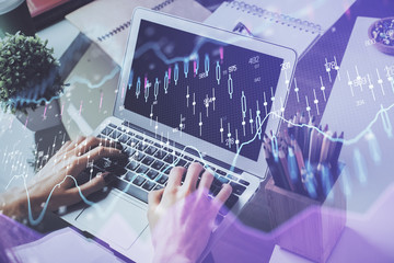 Double exposure of stock graph with businessman typing on computer in office on background. Concept of hard work.