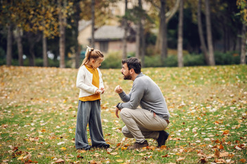 Devilish cute little girl with ponytail standing and looking at her father. Father crouching and...