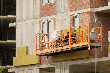 Two workers in a construction basket insulate the glassy wall of a multi-storey building. Safety measures at a construction site during high-altitude work. Thermal insulation of living spaces to save 