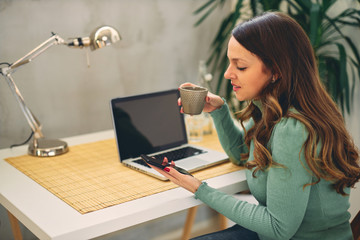 Obraz premium Young attractive female with coffee sitting in the modern office and having video call.