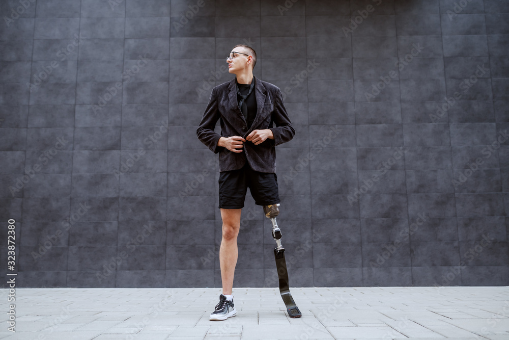 Canvas Prints Full length of handsome Caucasian businessman with artificial leg getting tired of work and taking of his tuxedo while standing outdoors in front of gray wall. It's time for sport.