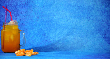A glass mug of citrus juice with ice and slices of ripe mandarin lie on a blue background. © Алексей Желтухин