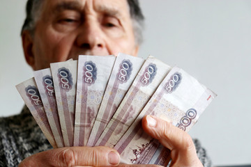 Elderly man counts russian rubles in hands. Pension payments, retirement savings or benefits concept, male pensioner with paper currency of Russia