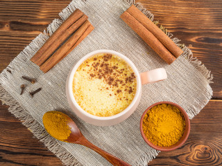 Top view of a cup of golden milk with turmeric and cinnamon on a wooden background