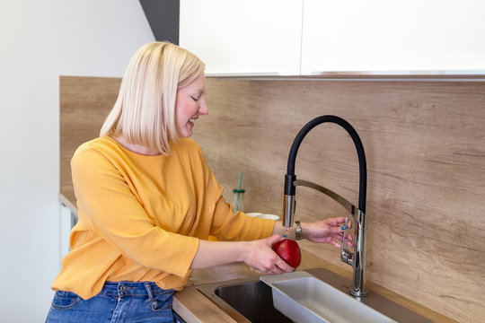 Cute girl washing apple in kitchen sink. Young Woman cleaning her fruit with water under the tap. Daily intake of vitamins with fruits, Diet and healthy eating