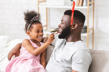 Little daughter putting make up on her laughing father