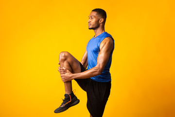 Young afro sportsman walks highly holding knee