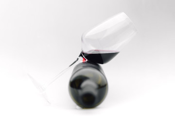 a glass of red wine lies on a bottle on a white background
